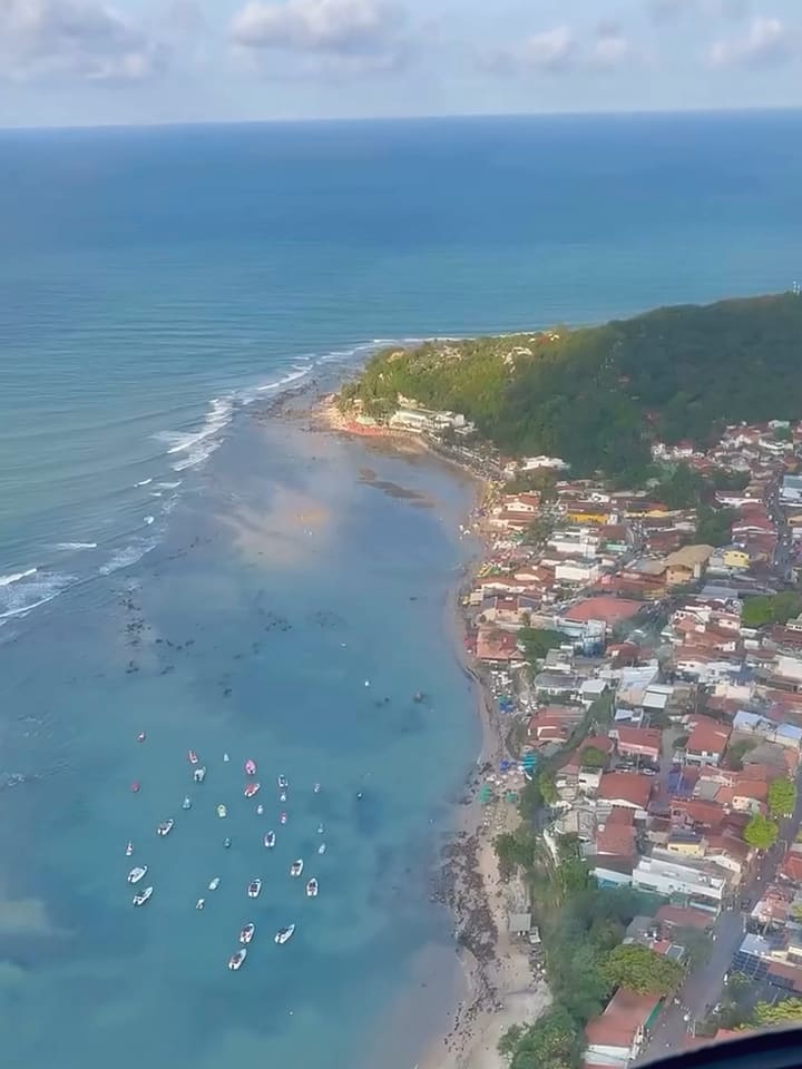 Vista aérea de Pipa, com a vila no alto das falésias e barcos na baía